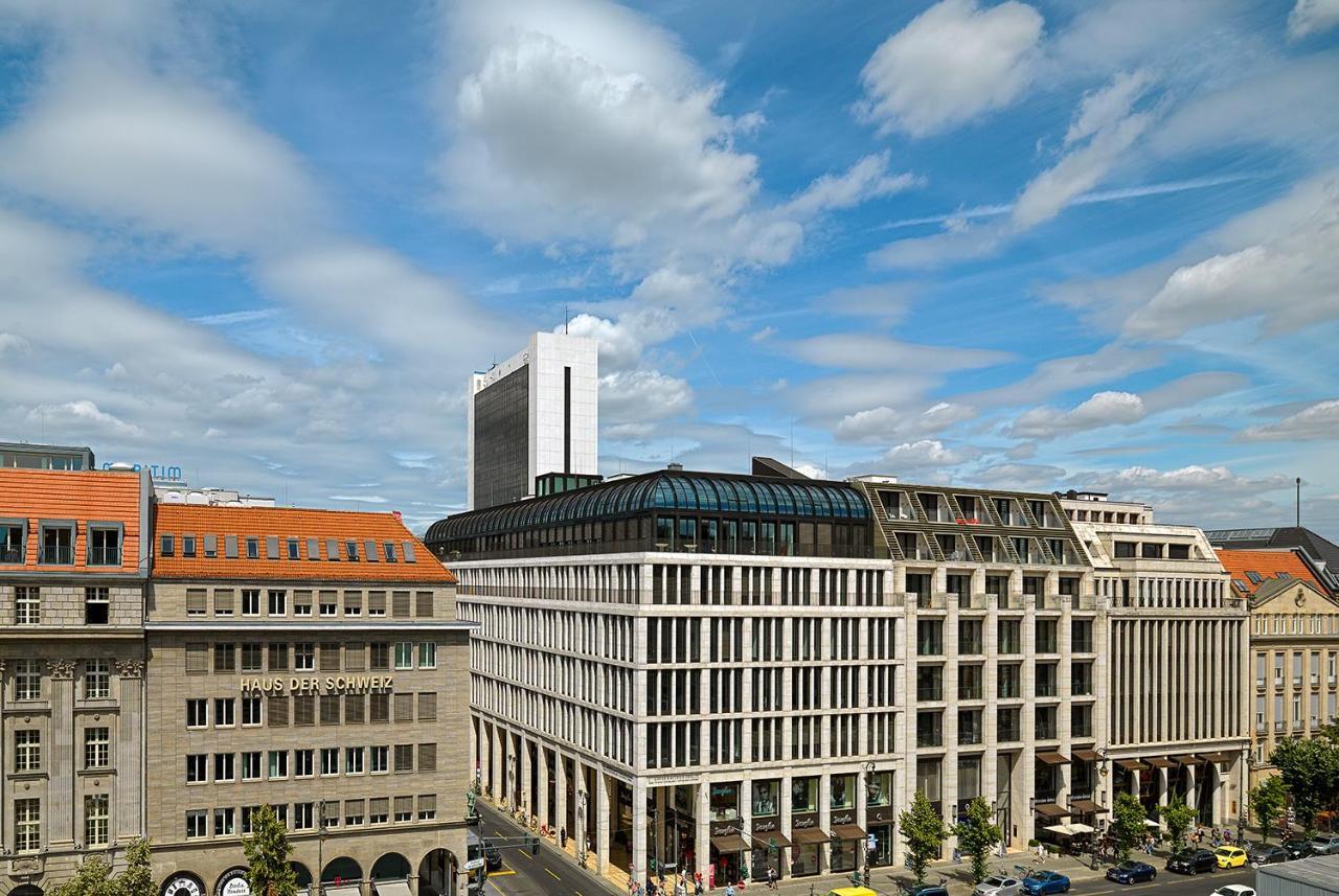 Hotel The Westin Grand Berlino Esterno foto The photo shows a modern urban landscape featuring a mix of architectural styles. In the foreground, a contemporary building with a large glass roof is prominently displayed, surrounded by other buildings that exhibit more traditional and historical 