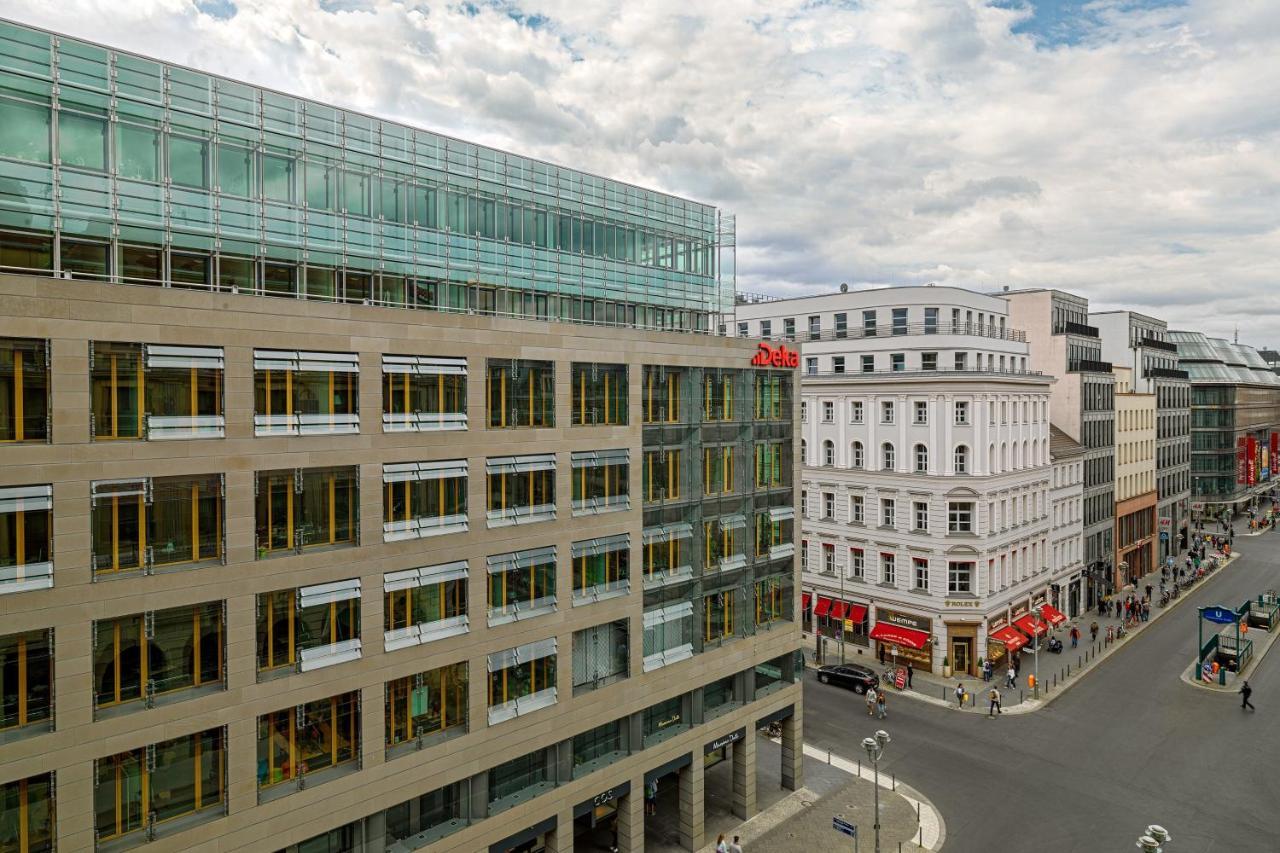 Hotel The Westin Grand Berlino Esterno foto The photo shows an urban scene featuring a modern building on the left side, which has a glass facade and a large entrance, suggesting it may be a commercial or office structure. Adjacent to it, there is another building with traditional architecture