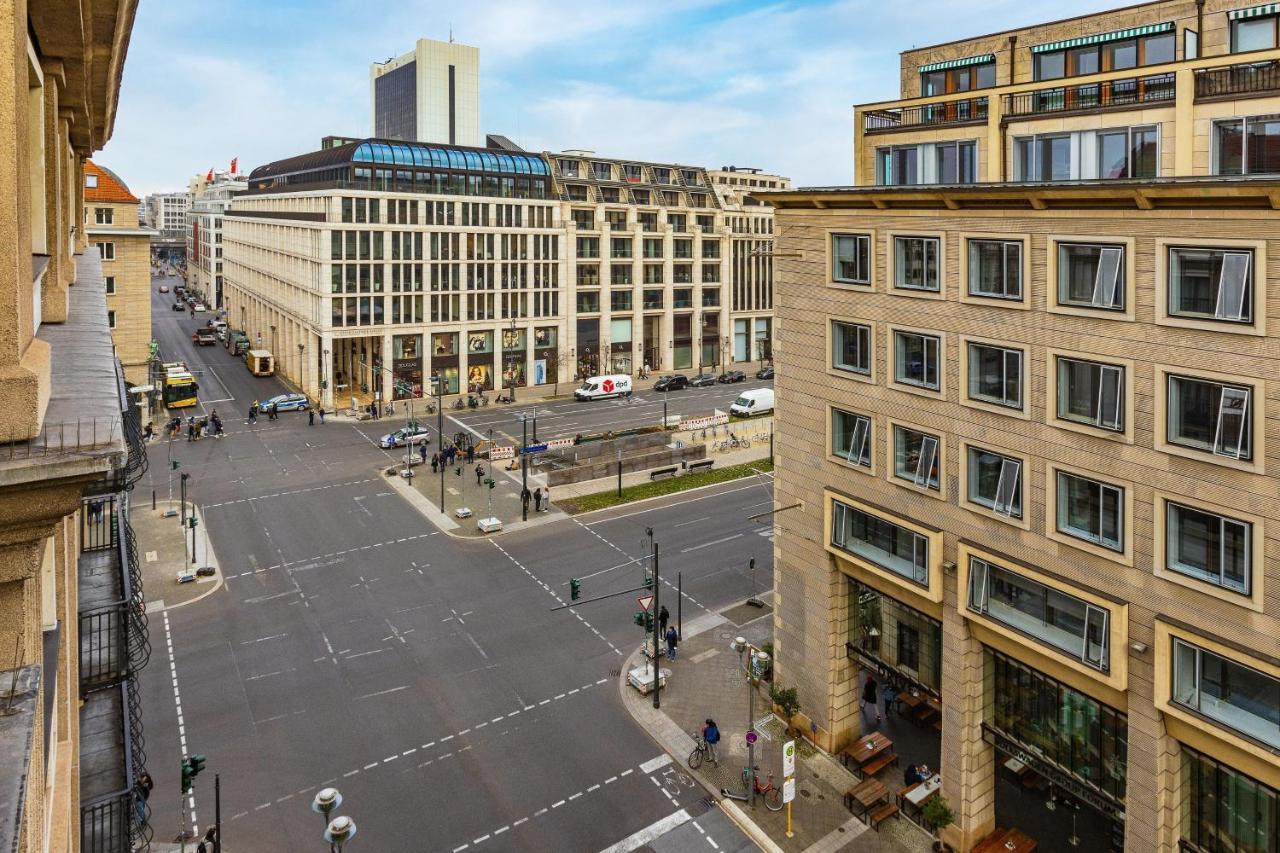 Hotel The Westin Grand Berlino Esterno foto The photo shows an urban scene featuring a street intersection surrounded by modern buildings. The architecture includes a mix of contemporary and classic styles. Vehicles are visible on the roads, and there are people walking on the sidewalks. The s