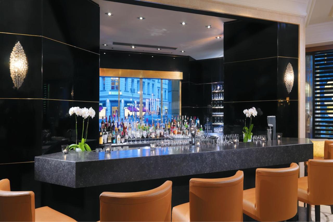 Hotel The Westin Grand Berlino Esterno foto The photo depicts a modern bar area with a sleek and elegant design. The bar counter is made of dark stone, and behind it is a well-stocked bar shelf featuring various bottles of alcohol. The backdrop is decorated with black panels, giving it a luxur