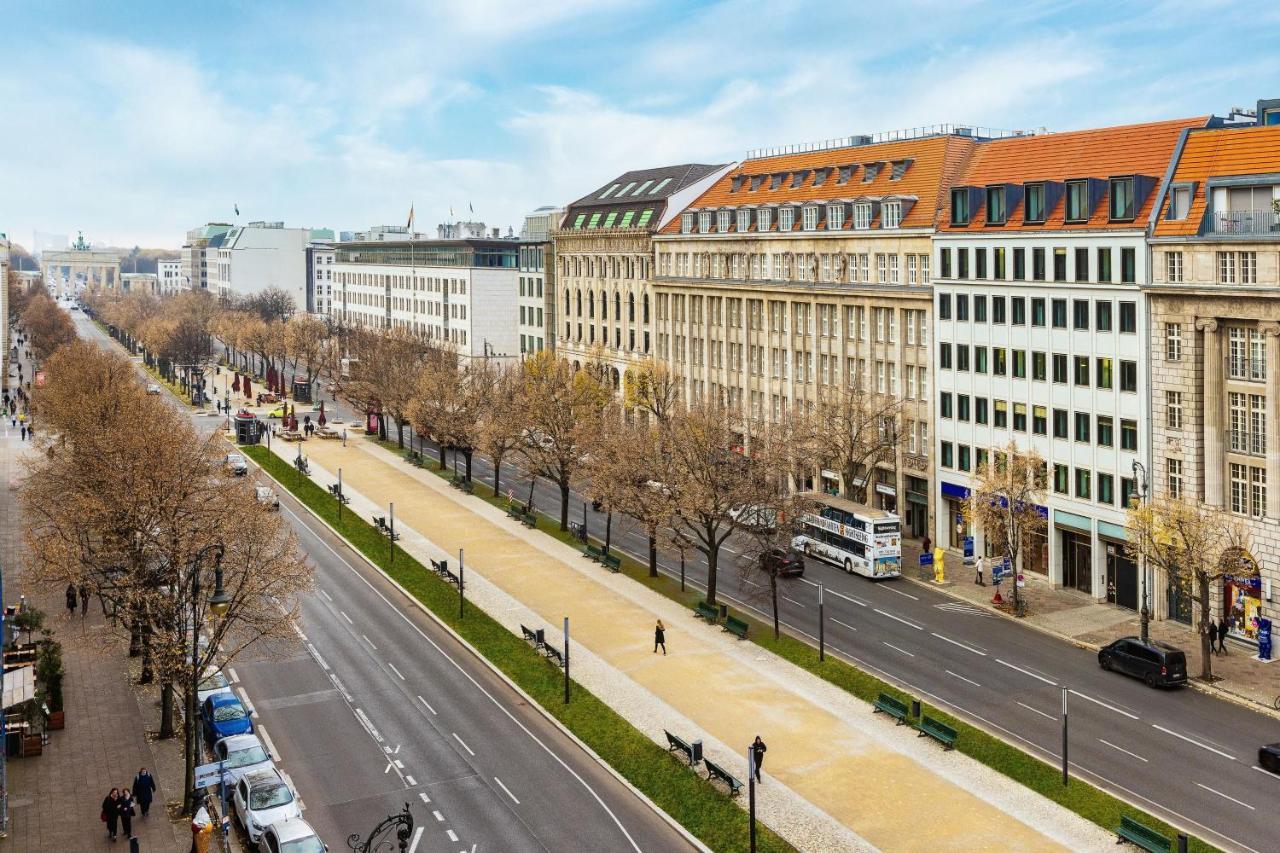 Hotel The Westin Grand Berlino Esterno foto The photo shows a wide street lined with buildings on either side. There are several trees, which seem to be bare, indicating a possibly early spring or late autumn setting. The architecture of the buildings is a mix of styles, with some appearing mo