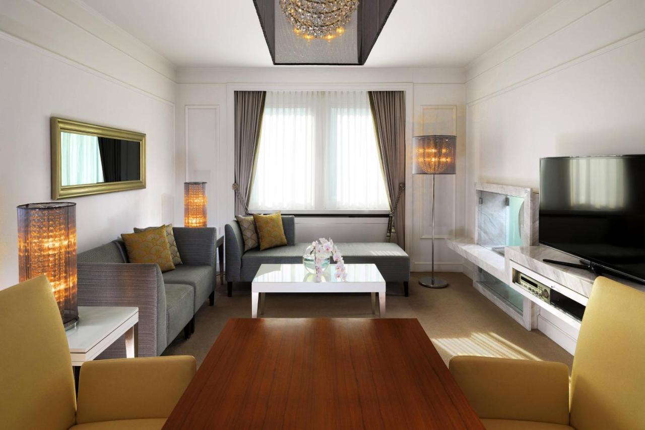 Hotel The Westin Grand Berlino Esterno foto The photo depicts a modern and elegantly designed living room. The space features:

- A comfortable seating area with a light gray sectional sofa and decorative cushions.
- A central white coffee table.
- Two stylish floor lamps adding warm lighting 