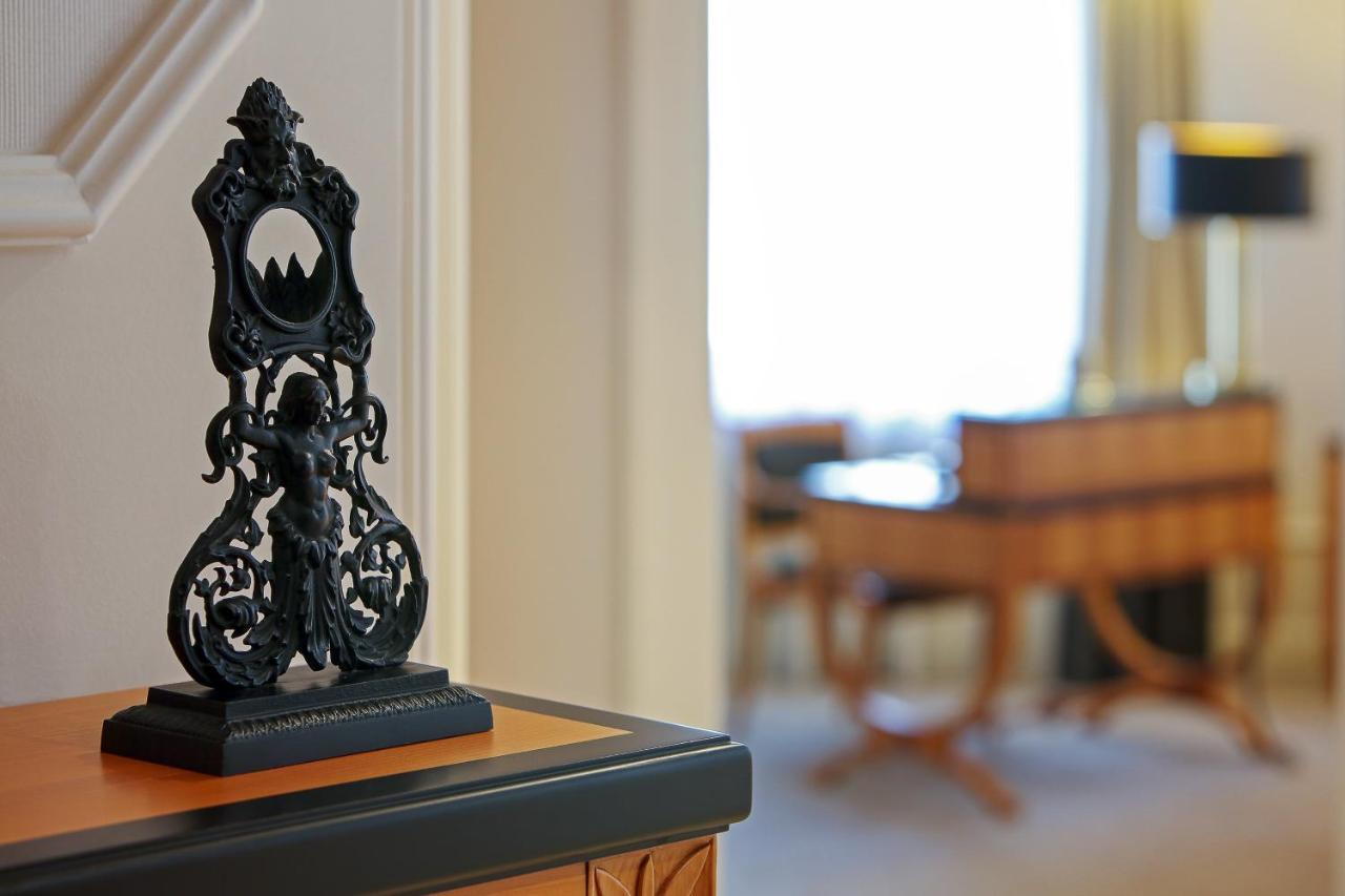 Hotel The Westin Grand Berlino Esterno foto The photo shows a decorative black object, possibly a sculpture or a stand, placed on a surface. The object features intricate designs, including a central figure and ornate detailing. In the background, there is a blurred view of a room with light-c