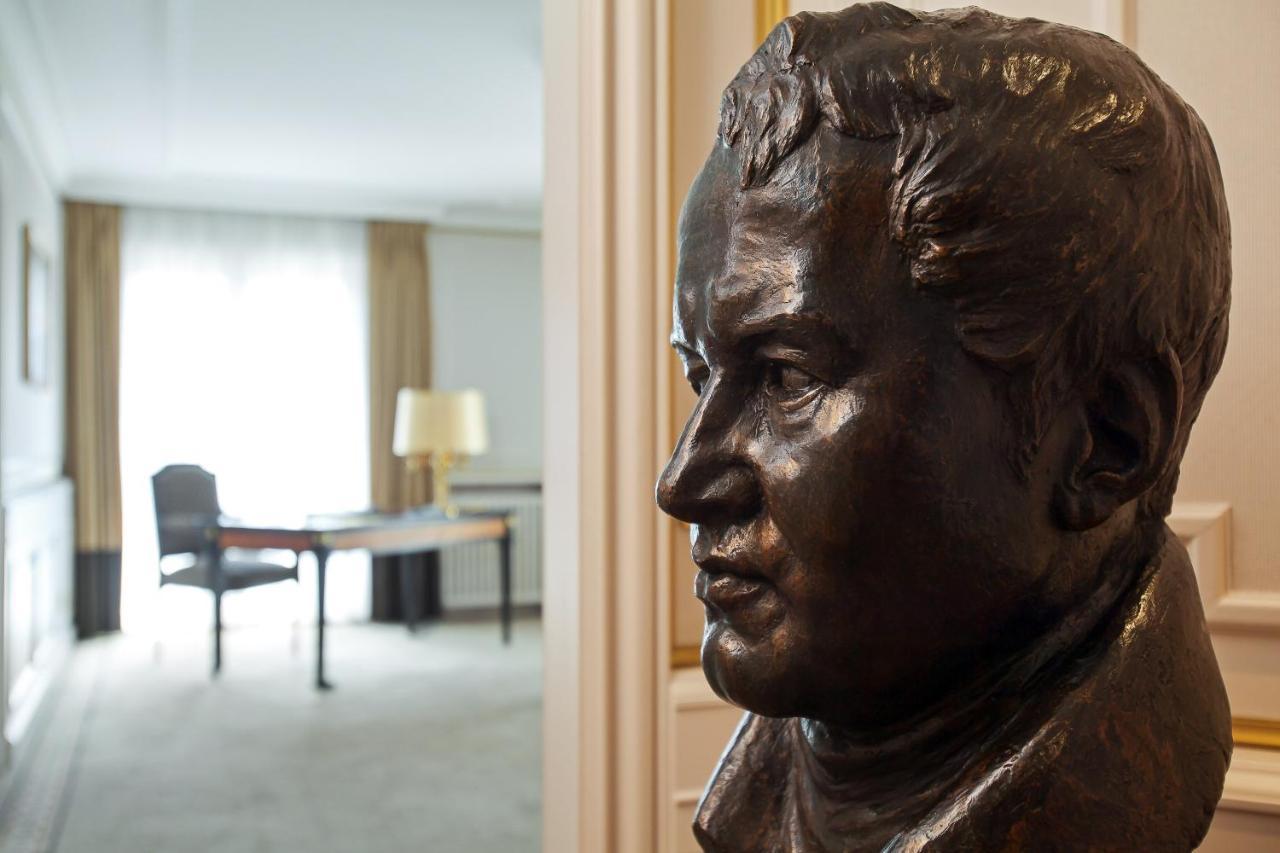 Hotel The Westin Grand Berlino Esterno foto The photo shows a bronze bust of a man, likely depicting a historical figure, with a focus on his face in profile. In the background, there is a well-lit room featuring a table and chair, indicating a comfortable and professional setting. The presenc