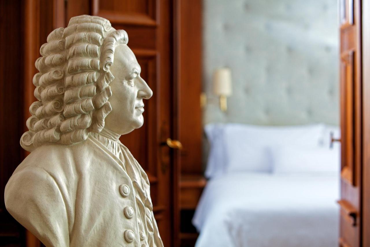 Hotel The Westin Grand Berlino Esterno foto The image features a bust of a historical figure, likely a musician or composer, set against a background that includes a softly lit bedroom with a neatly made bed. The bust is intricately detailed, showcasing the figure's hairstyle and clothing typi