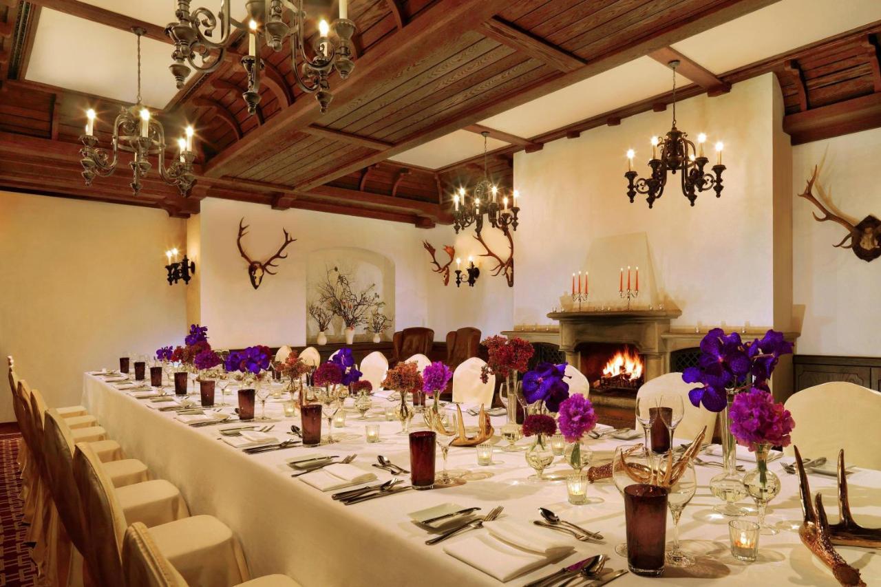 Hotel The Westin Grand Berlino Esterno foto The photo depicts an elegantly arranged dining room. A long table is set with white tablecloths and neatly arranged place settings featuring glassware and cutlery. Vibrant purple flowers are placed in vases at intervals along the table, adding a pop 