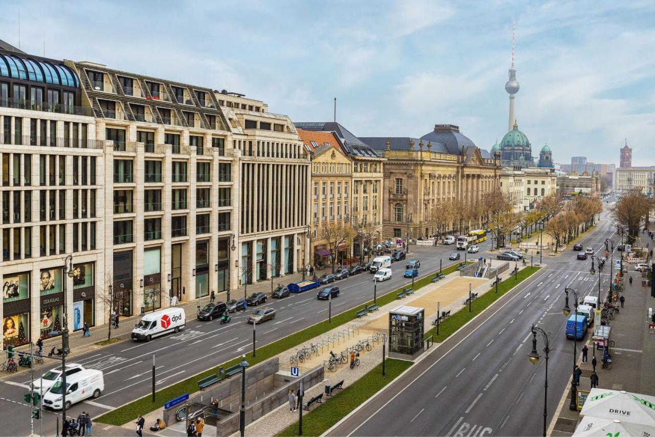Hotel The Westin Grand Berlino Esterno foto The photo shows a wide urban street with a mix of modern and historic buildings on either side. The foreground features a wide road with traffic, including cars and vans. On the left, there are contemporary architectural designs, while on the right, 