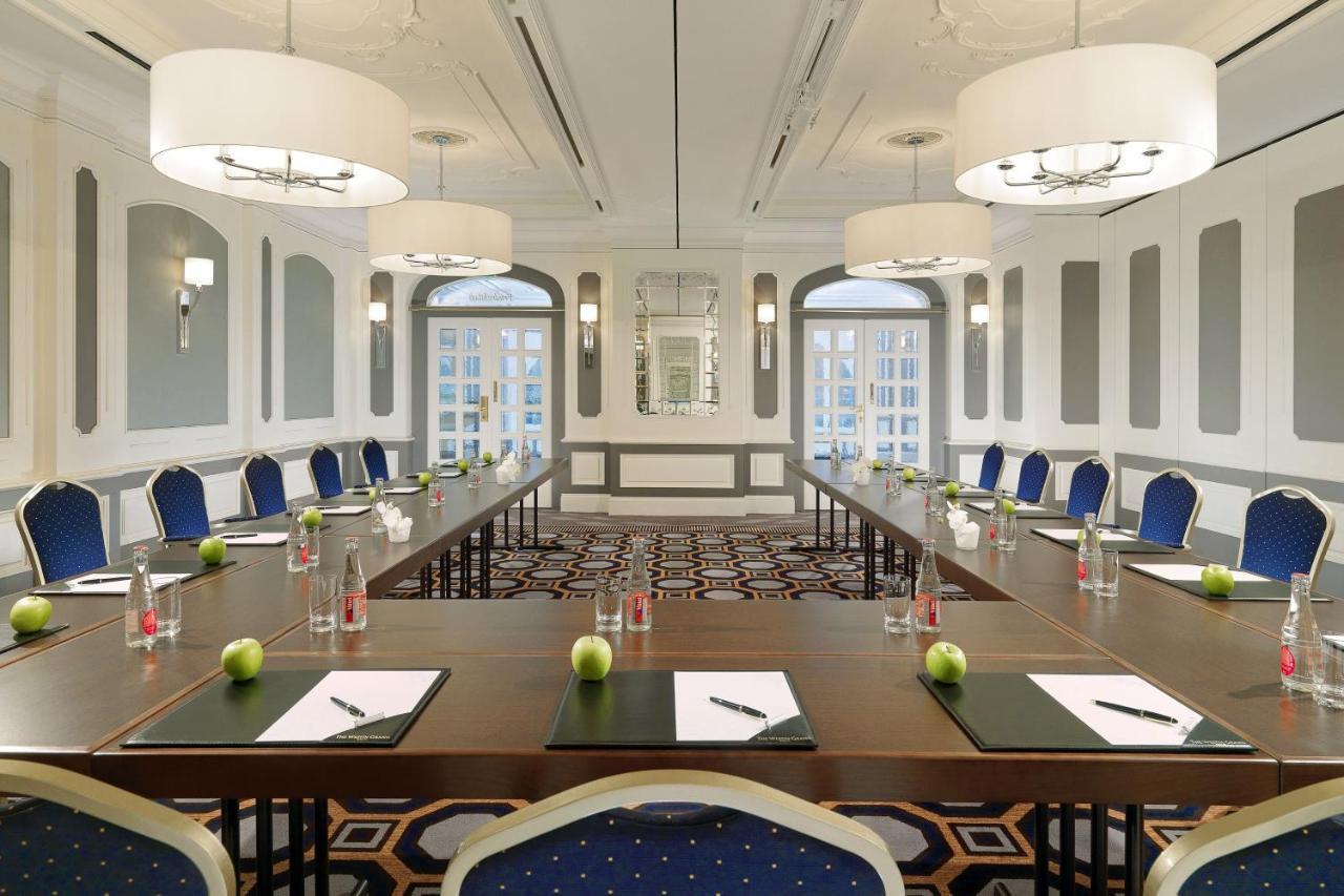 Hotel The Westin Grand Berlino Esterno foto The image shows a well-lit conference room designed for meetings. It features a long rectangular table surrounded by chairs, all elegantly arranged. On the table, there are notepads, pens, and bottles of water, along with green apples placed at inter