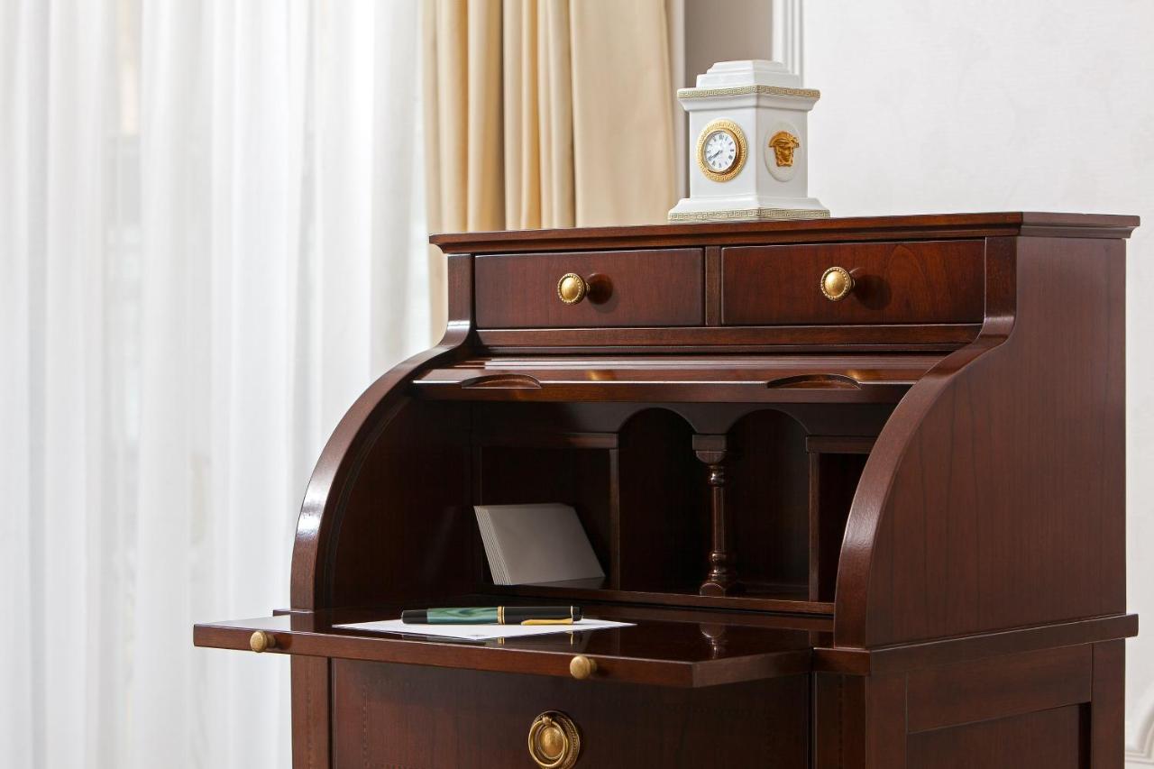 Hotel The Westin Grand Berlino Esterno foto The image shows a wooden writing desk with a rich, dark finish. The desk features a curved front and an open compartment above a flat writing surface. There are two small drawers at the top, each with round brass handles. On the desk, there is a shee