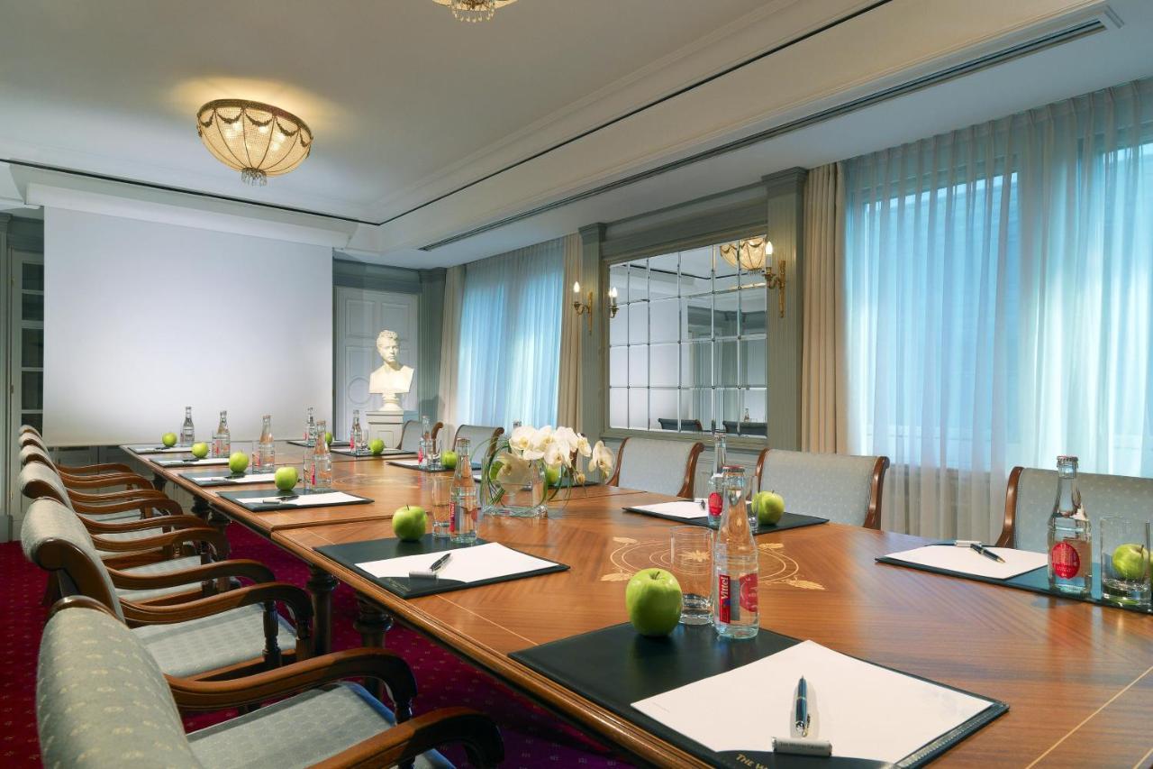 Hotel The Westin Grand Berlino Esterno foto The photo depicts a stylish and well-lit conference room. In the center, there is a large wooden table arranged with several items, including notepads and pens at each seat, along with green apples and bottles of water. The room features elegant furn