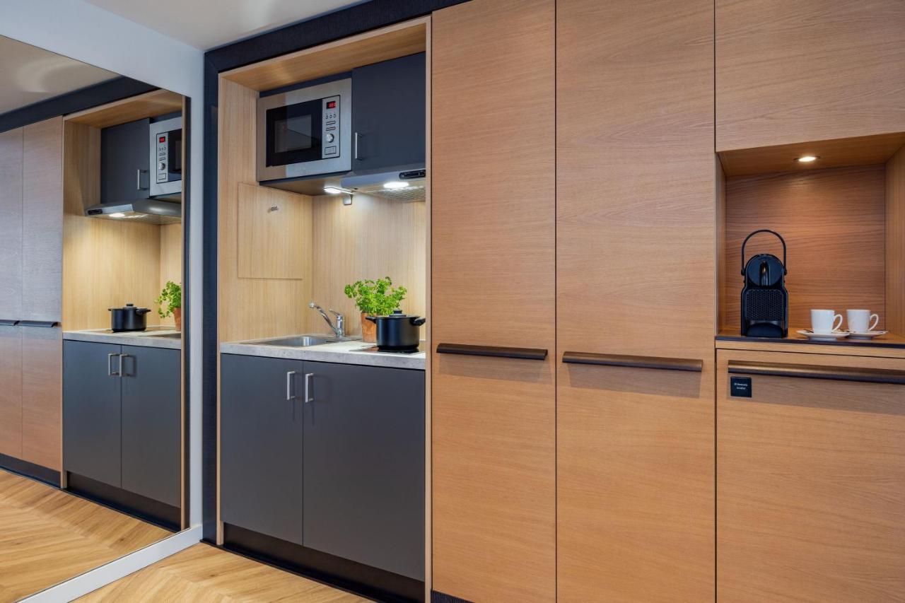 Hotel The Westin Grand Berlino Esterno foto The photo shows a modern kitchen area with a sleek design. It features built-in cabinetry with a mix of light wood and dark grey finishes. There is a stainless steel microwave mounted above a countertop that includes a small sink. A small indoor plan
