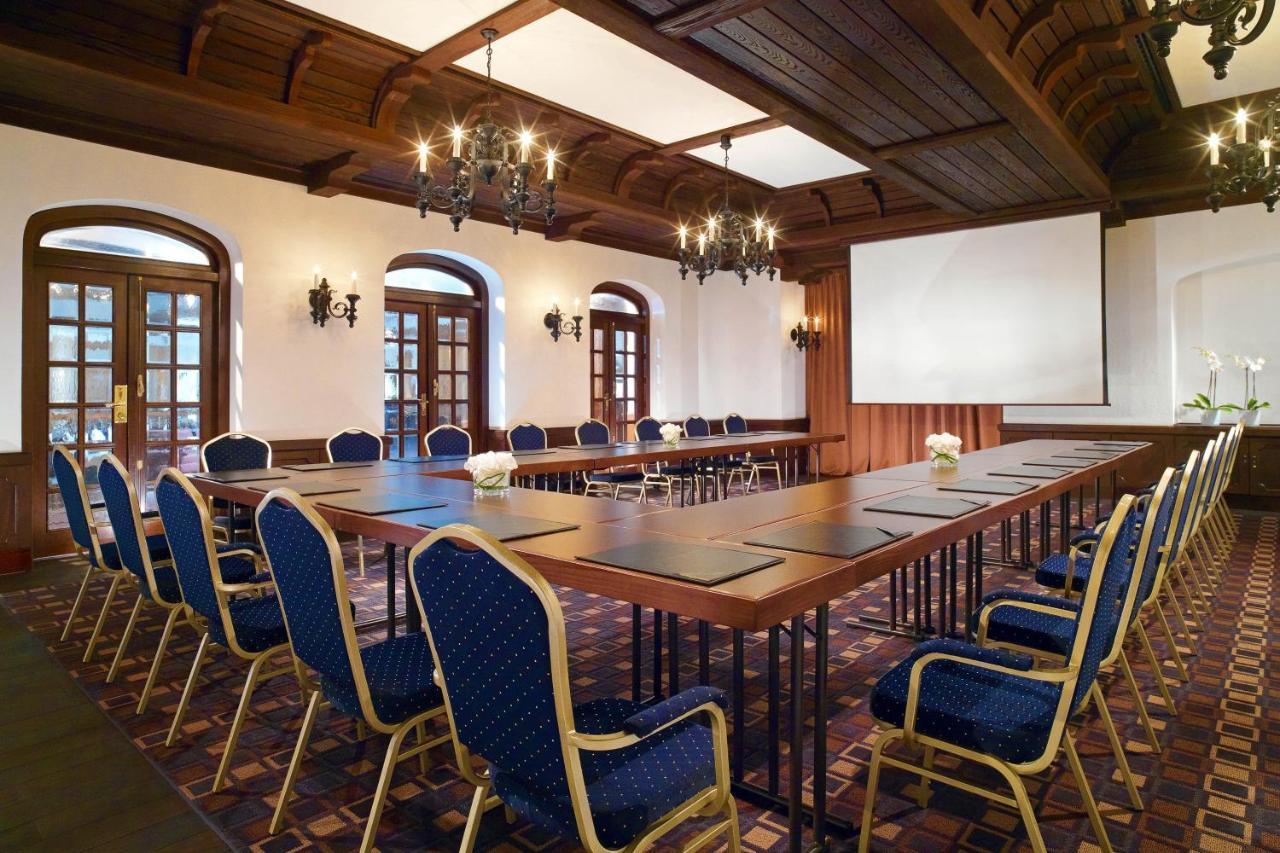 Hotel The Westin Grand Berlino Esterno foto The photo shows a conference room with an elegant design. There is a long rectangular table set up in the center, surrounded by upholstered chairs with blue fabric. The room features wooden ceiling beams and decorative lighting fixtures, including ch