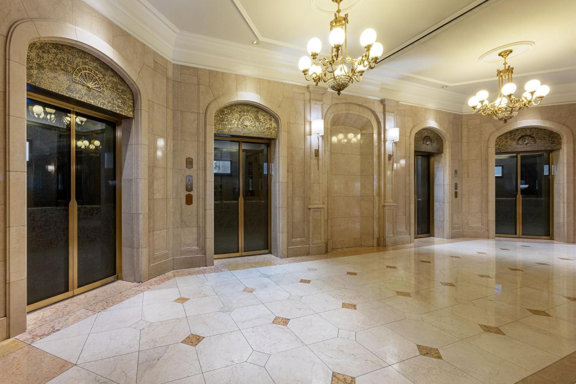 Hotel The Westin Grand Berlino Esterno foto The photo shows an elegant lobby area with several glass elevators. The walls are finished with light-colored stone, giving a polished and upscale look. The ceiling features ornate chandeliers that add to the luxurious atmosphere. The floor is tiled 